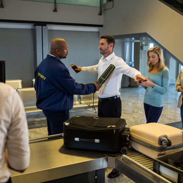 Security guard frisk passengers standing in queue at airport terminal